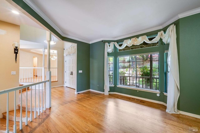 spare room with crown molding, baseboards, a chandelier, visible vents, and wood finished floors