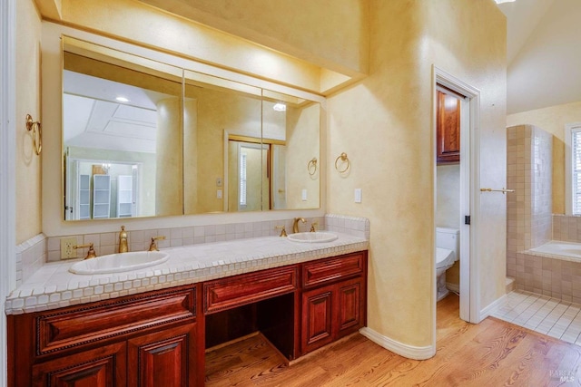 bathroom featuring a relaxing tiled tub, toilet, a sink, and wood finished floors