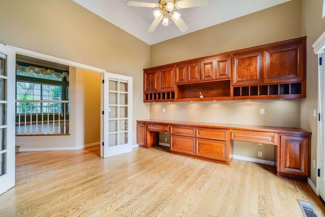 unfurnished office with baseboards, built in desk, light wood-style flooring, and a ceiling fan