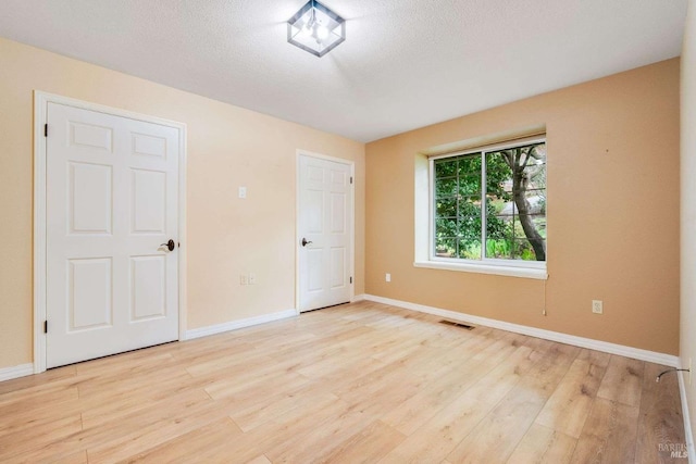 spare room with baseboards, visible vents, light wood-style floors, and a textured ceiling