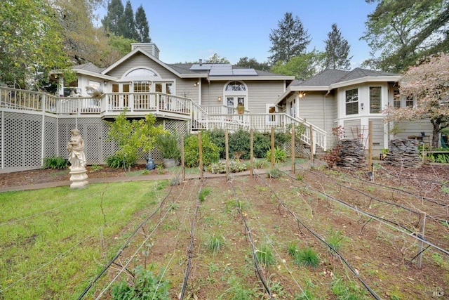 back of property with solar panels, a wooden deck, stairway, and a yard