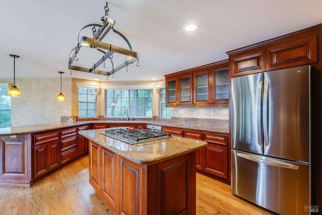 kitchen with light wood-style flooring, light stone countertops, a kitchen island, appliances with stainless steel finishes, and a sink