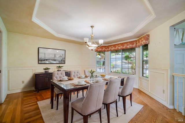 dining space with light wood finished floors, wainscoting, a raised ceiling, and an inviting chandelier