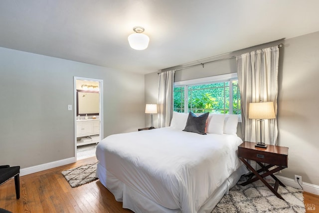 bedroom featuring baseboards, a sink, ensuite bath, and hardwood / wood-style flooring
