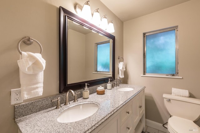 bathroom with double vanity, toilet, baseboards, and a sink