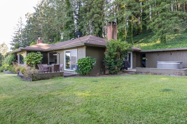 back of property with a chimney, a hot tub, a yard, a patio, and stucco siding