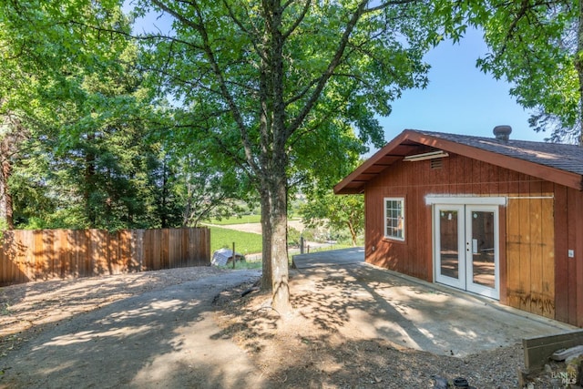 exterior space featuring a shingled roof, a patio area, fence, and french doors
