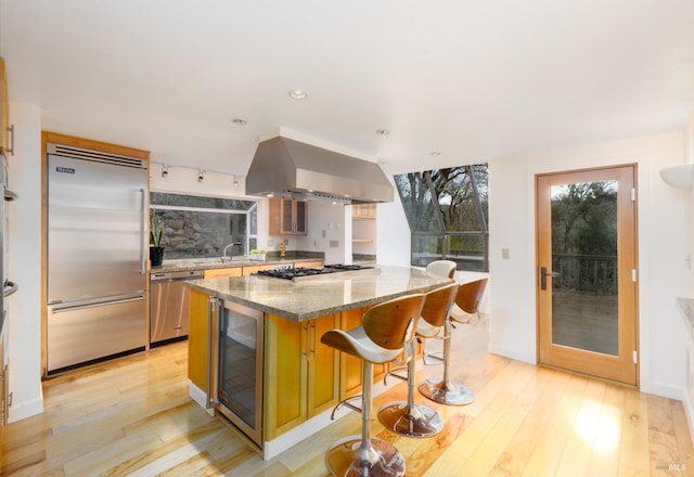 kitchen featuring wall chimney range hood, a center island, a breakfast bar area, stainless steel appliances, and wine cooler