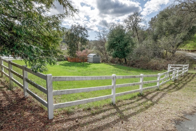 view of gate featuring a storage shed, an outbuilding, fence, a rural view, and a lawn