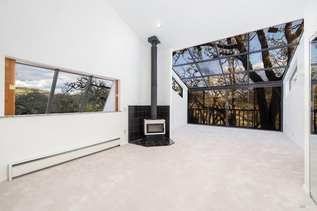 unfurnished living room featuring plenty of natural light, high vaulted ceiling, baseboard heating, carpet floors, and a wood stove