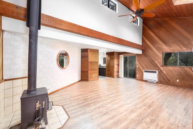 unfurnished living room featuring high vaulted ceiling, a ceiling fan, wood finished floors, heating unit, and a wood stove