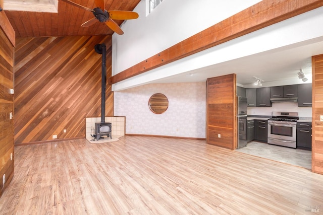 unfurnished living room with wooden walls, a wood stove, a ceiling fan, light wood-style floors, and baseboards