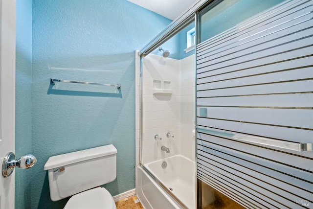 bathroom featuring a textured wall, combined bath / shower with glass door, and toilet