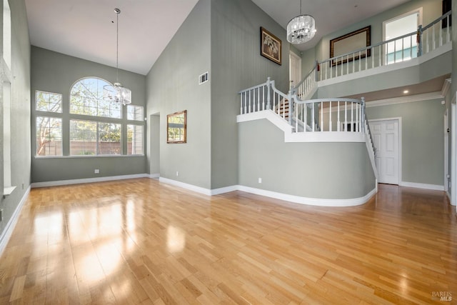 unfurnished living room featuring wood finished floors, a high ceiling, a chandelier, and stairway