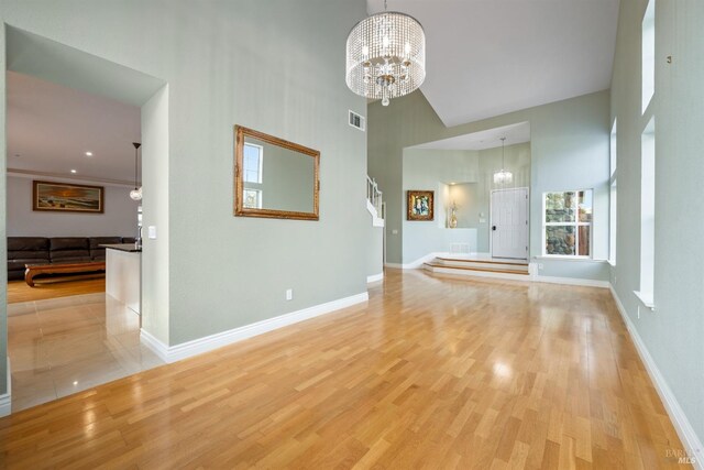 unfurnished living room featuring visible vents, baseboards, a high ceiling, light wood finished floors, and a notable chandelier