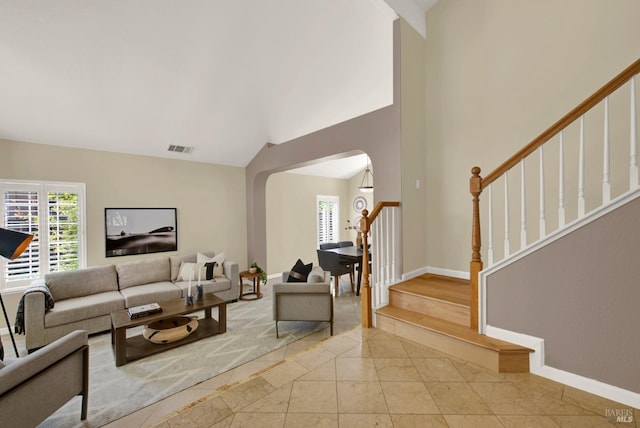 living area with stairway, high vaulted ceiling, baseboards, arched walkways, and visible vents