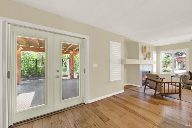 doorway to outside with baseboards, light wood-type flooring, a tiled fireplace, and french doors