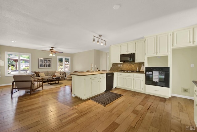 kitchen with a sink, light wood finished floors, a peninsula, black appliances, and decorative backsplash