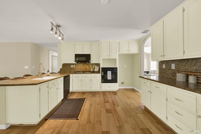 kitchen with a sink, arched walkways, light wood-style floors, a peninsula, and black appliances