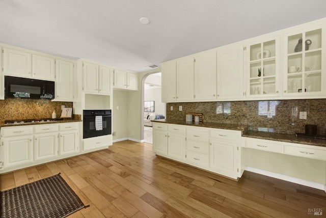 kitchen featuring light wood-style floors, arched walkways, black appliances, and decorative backsplash