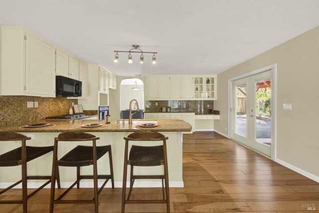kitchen featuring a sink, black microwave, tasteful backsplash, wood-type flooring, and a peninsula
