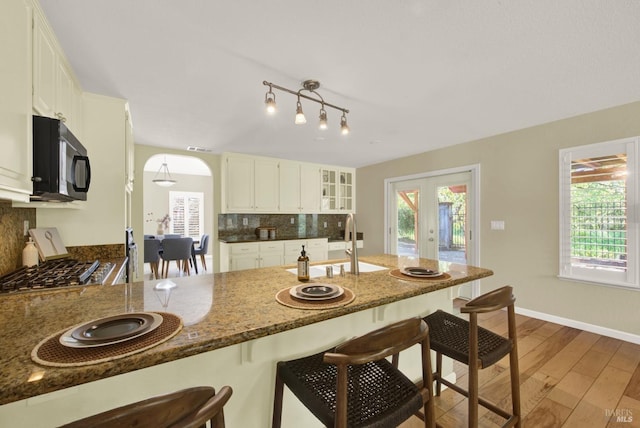 kitchen featuring a wealth of natural light, black microwave, wood finished floors, a breakfast bar, and decorative backsplash