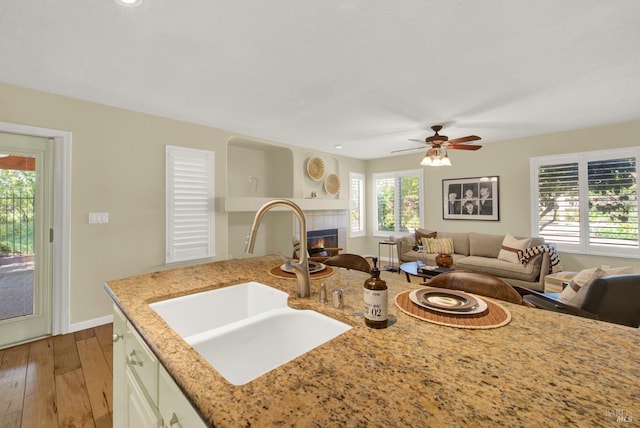 kitchen featuring a fireplace, light stone counters, a sink, open floor plan, and wood-type flooring