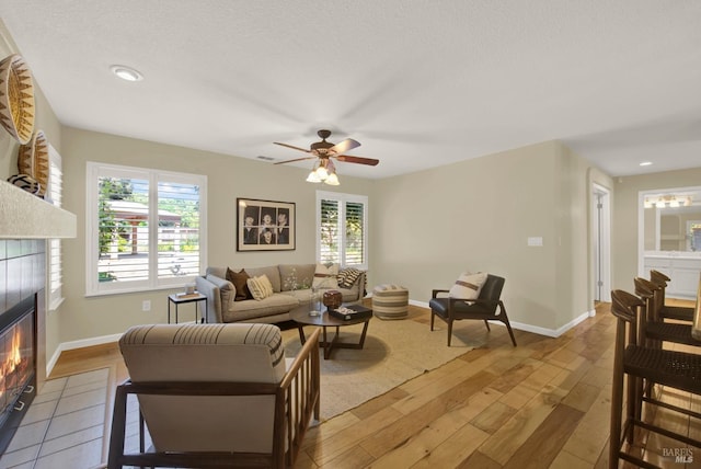 living area with baseboards, a tile fireplace, a ceiling fan, and hardwood / wood-style flooring