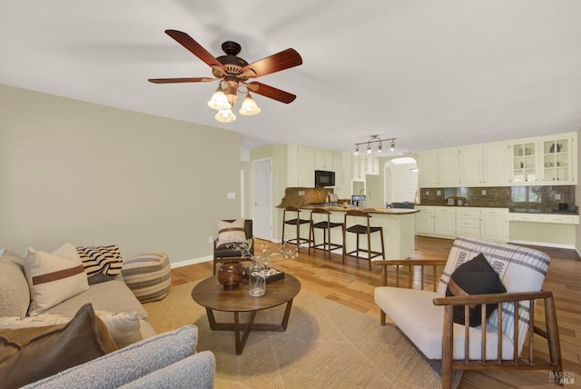 living area featuring arched walkways, baseboards, light wood-style floors, and a ceiling fan