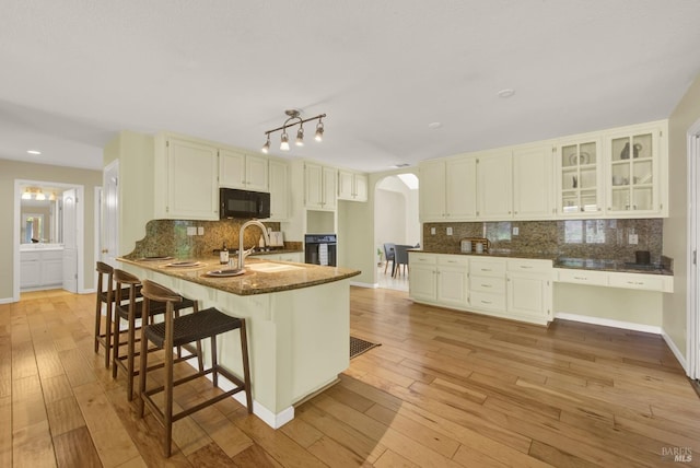 kitchen featuring arched walkways, light wood-style flooring, black appliances, and a peninsula