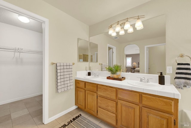 bathroom with baseboards, double vanity, a sink, and tile patterned flooring