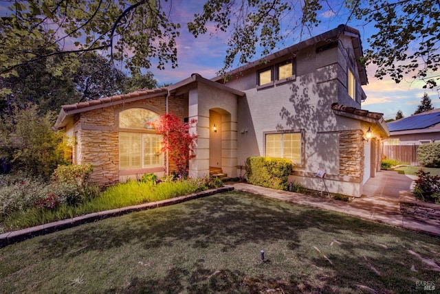 view of front of property featuring stone siding, fence, a front yard, and stucco siding
