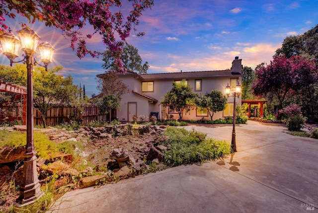 view of front of house featuring a tile roof, concrete driveway, stucco siding, fence, and a chimney