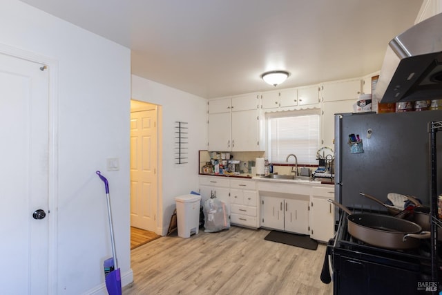 kitchen featuring light wood-type flooring, white cabinets, a sink, and freestanding refrigerator