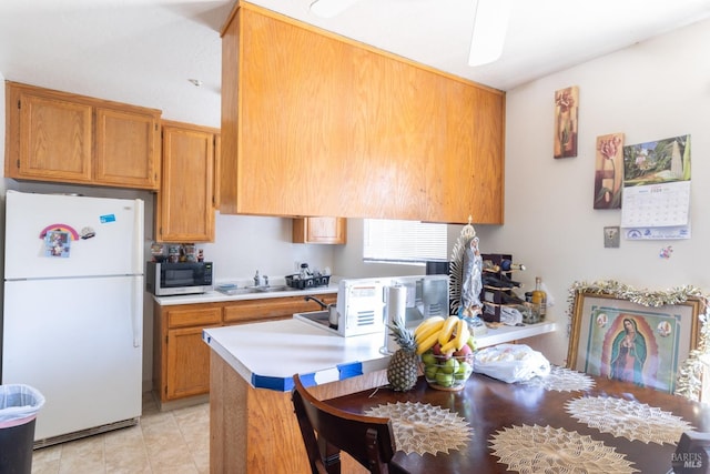 kitchen with light countertops, stainless steel microwave, a sink, freestanding refrigerator, and brown cabinets