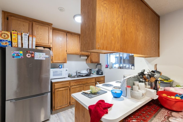 kitchen featuring light countertops, brown cabinets, a sink, white microwave, and freestanding refrigerator