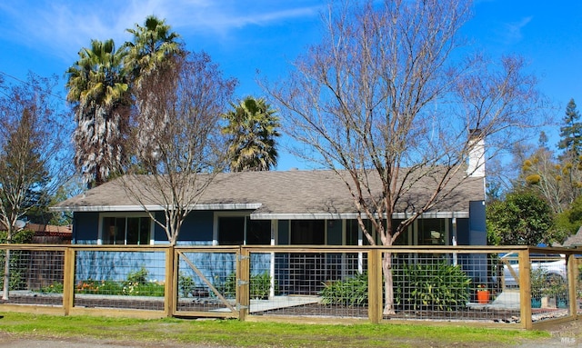 rear view of house with a shingled roof, a chimney, and fence