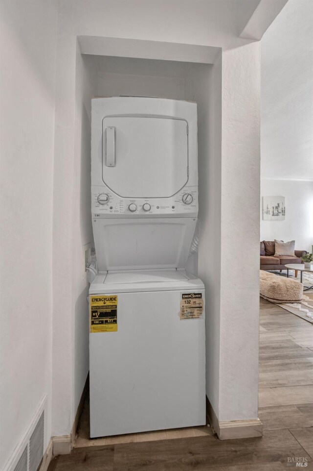 laundry room with stacked washing maching and dryer, wood finished floors, laundry area, and visible vents