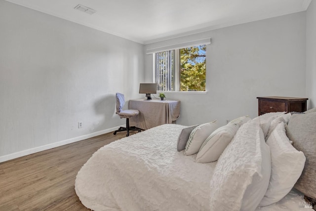 bedroom with ornamental molding, visible vents, baseboards, and wood finished floors