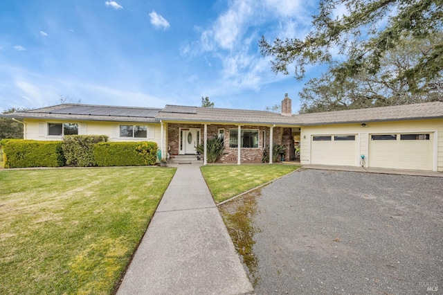 ranch-style home with an attached garage, aphalt driveway, a front lawn, solar panels, and a chimney