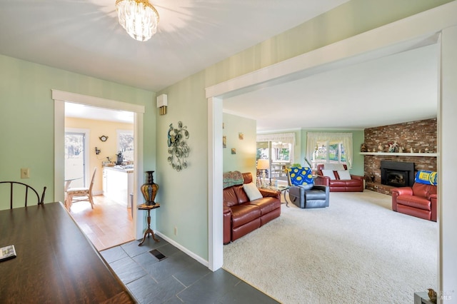 living area featuring baseboards, a wealth of natural light, dark carpet, and a brick fireplace
