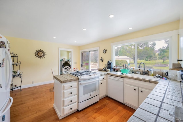 kitchen with white appliances, tile countertops, light wood-style floors, and a peninsula