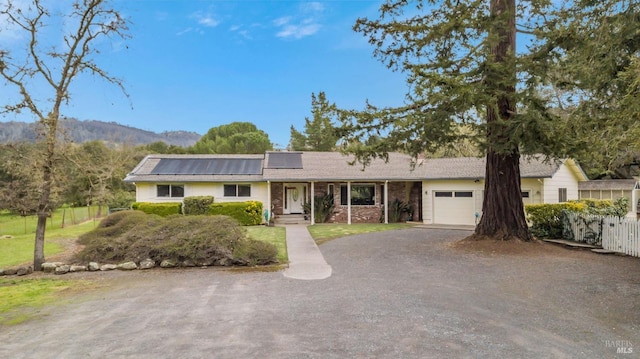 ranch-style house featuring fence, roof mounted solar panels, driveway, and an attached garage