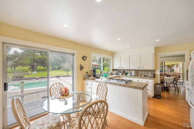 interior space with tile counters, white gas cooktop, light wood-style flooring, white cabinets, and a peninsula