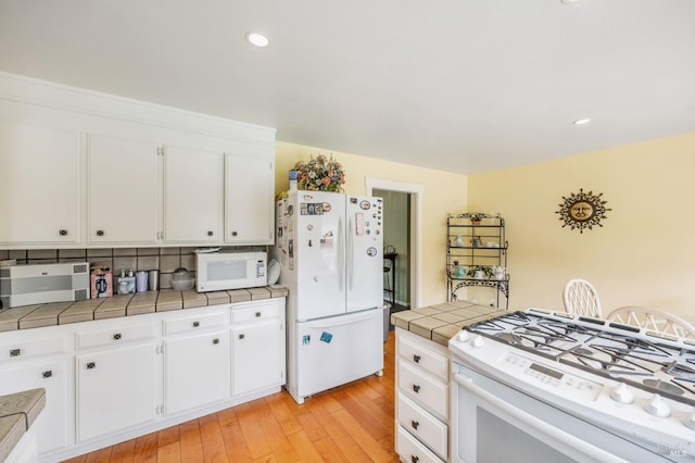 kitchen featuring white cabinets, tile counters, light wood finished floors, and white appliances