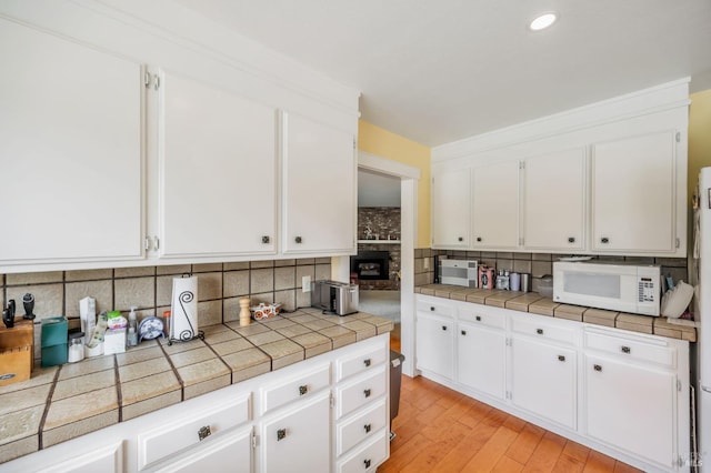 kitchen with tasteful backsplash, recessed lighting, light wood-style floors, white cabinets, and white microwave