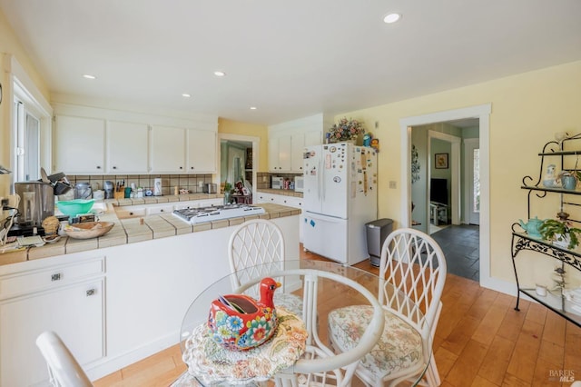 kitchen featuring tile counters, light wood-type flooring, white appliances, white cabinets, and a peninsula