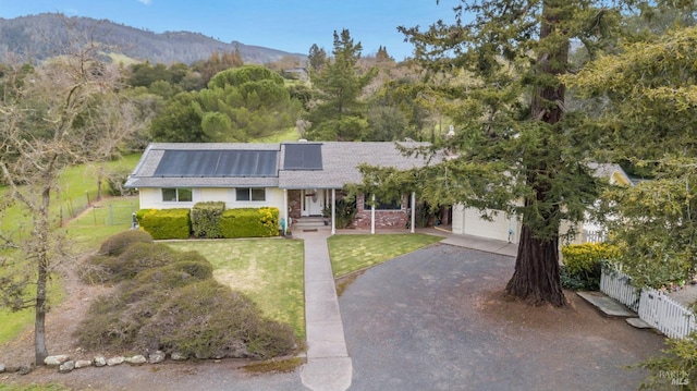 ranch-style home featuring roof with shingles, fence, aphalt driveway, a front lawn, and solar panels