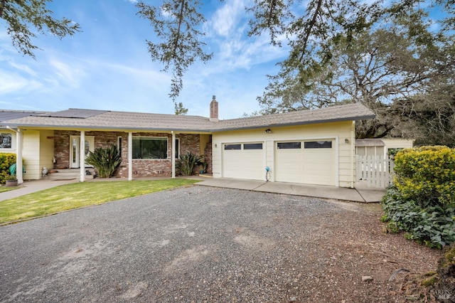 single story home with a chimney, fence, driveway, a garage, and roof mounted solar panels