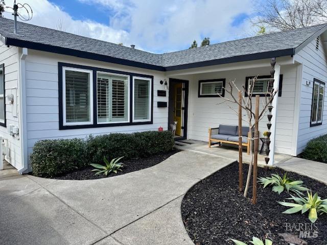 single story home with an AC wall unit, a porch, and roof with shingles